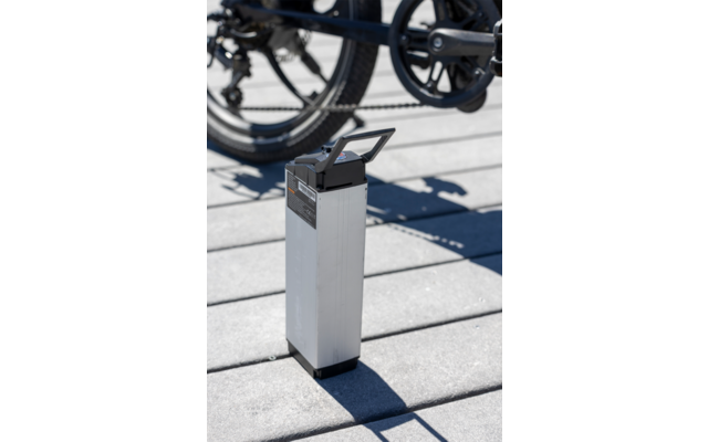 Witte rechthoekige e-bike accu op grijze grond met fietswielen op de achtergrond