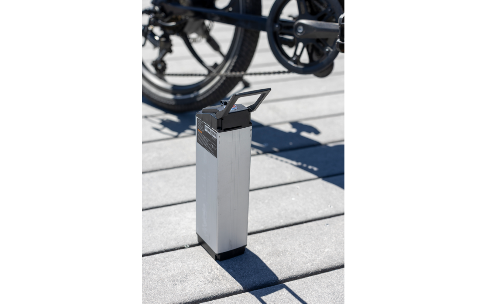 Witte rechthoekige e-bike accu op grijze grond met fietswielen op de achtergrond