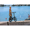 Vrouw met fiets staat op een havenmuur, water en boten op de achtergrond