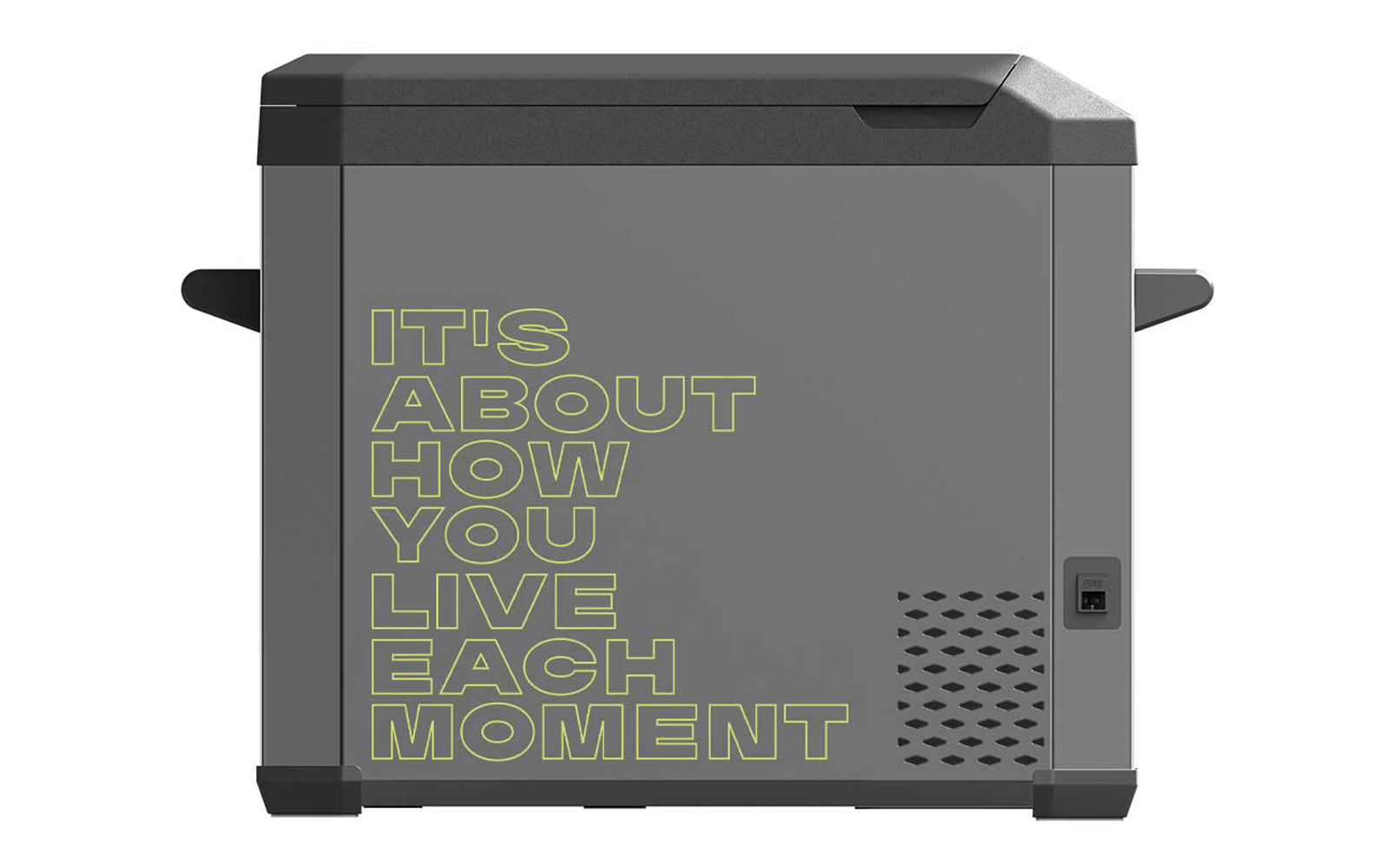 Graue rechteckige Box mit aufgedrucktem Text "IT'S ABOUT HOW YOU LIVE EACH MOMENT" in gelbgrüner Konturschrift, seitliche Griffe, Lüftungslöcher und kleiner rechteckiger Anschluss rechts