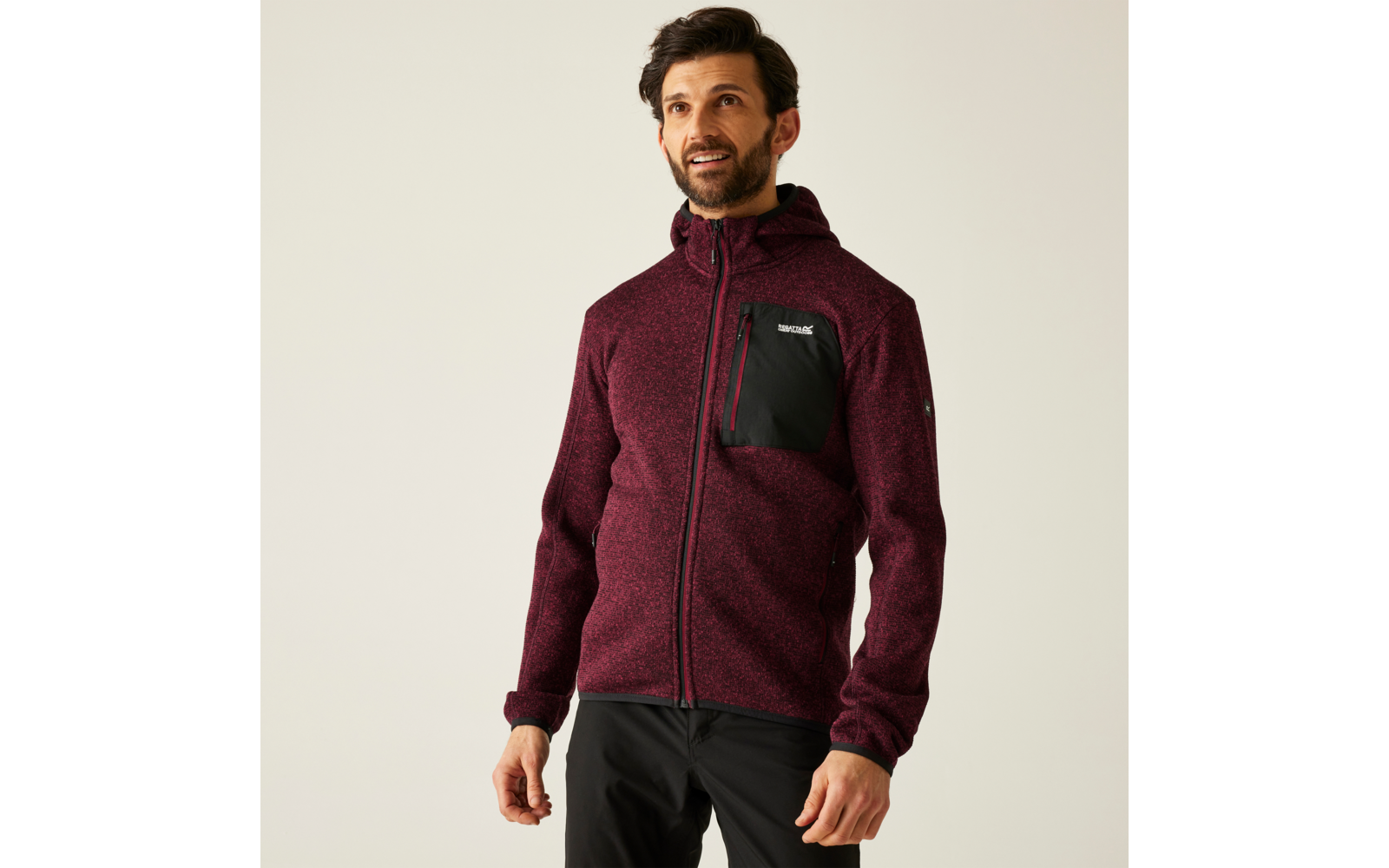 Mann trägt eine bordeauxrote Jacke mit schwarzer Brusttasche und steht vor hellem Hintergrund