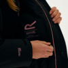 Person öffnet die Innenseite einer schwarzen Jacke, auf der ein Logo und Text sichtbar sind