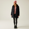 Frau trägt rosa Mütze, schwarzer Mantel, rosa Pullover, schwarze Hose und schwarze Schuhe vor hellem Hintergrund