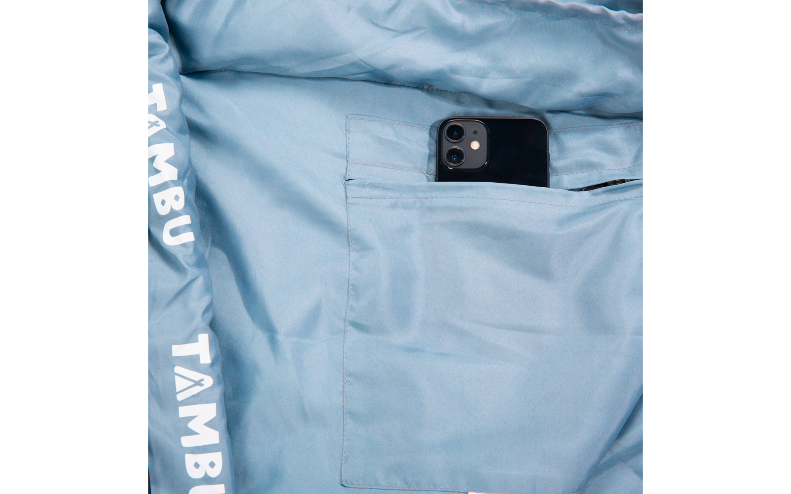 Light blue jacket lining with an inner pocket holding a black smartphone; white text 'TAMBU' on the hem