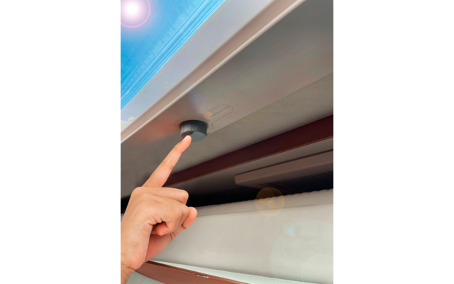 Hand zeigt auf einen grauen Knopf an einer weißen Decke mit blauem Himmel im Hintergrund