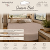 Binnenopname van een slaapgedeelte in een voertuig met een rond queenbed, lichtbeige hoeslaken, drie kussens, raam met boszicht, nachtkastje met potplant en productlogo/tekst op het beeld