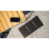 Ein faltbares Solarpanel liegt auf einem grauen Boden neben einem Holztisch mit einem Kabel und einem Stecker