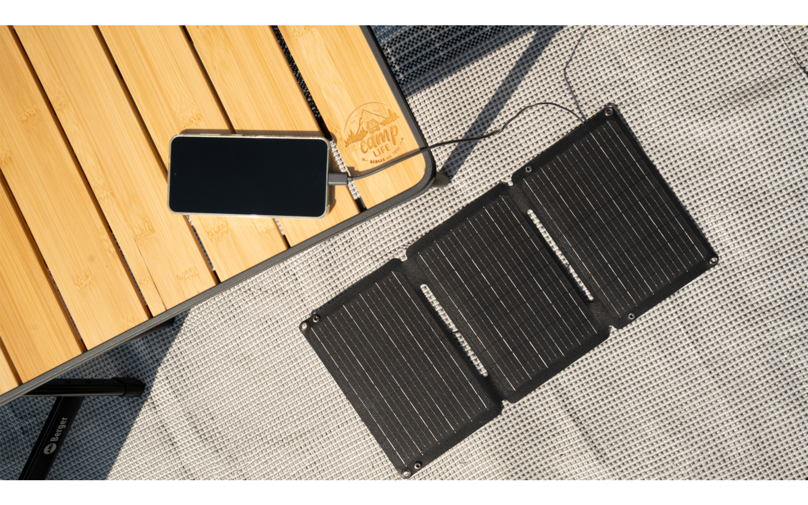 Ein faltbares Solarpanel liegt auf einem grauen Boden neben einem Holztisch mit einem Kabel und einem Stecker