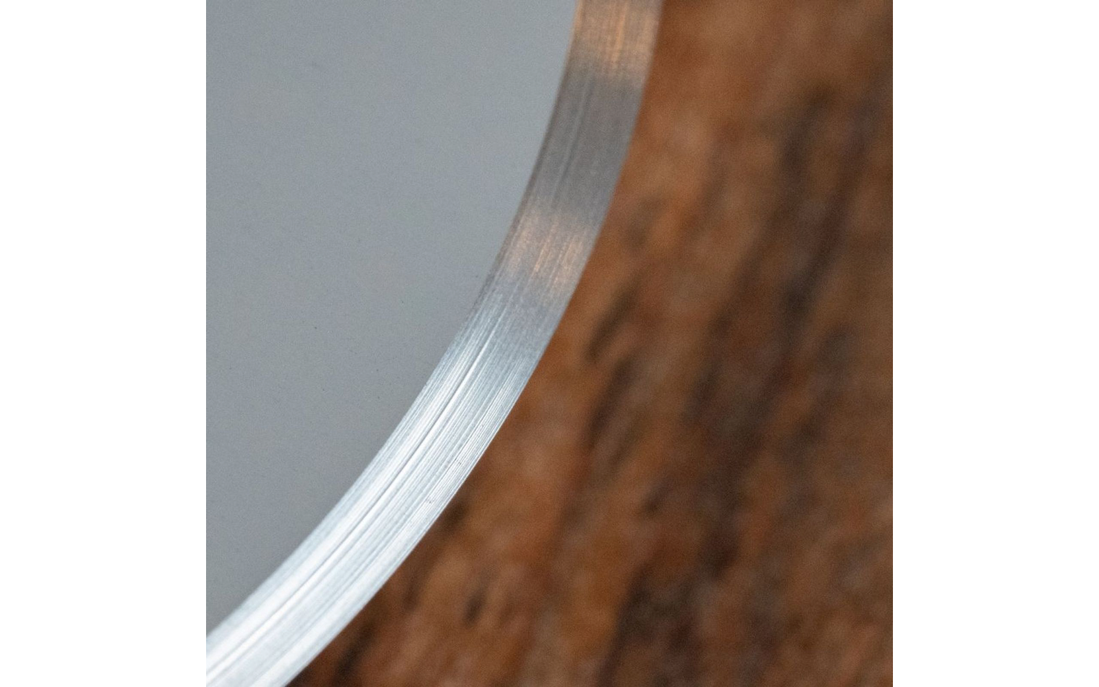 Gros plan d'un bord métallique courbé avec de fines rayures sur une surface en bois, fond gris