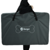 Large dark gray rectangular carrying bag with two black handles and a white Berger logo inside a bone-shaped outline; person partially visible (torso and arm in black clothing); white background