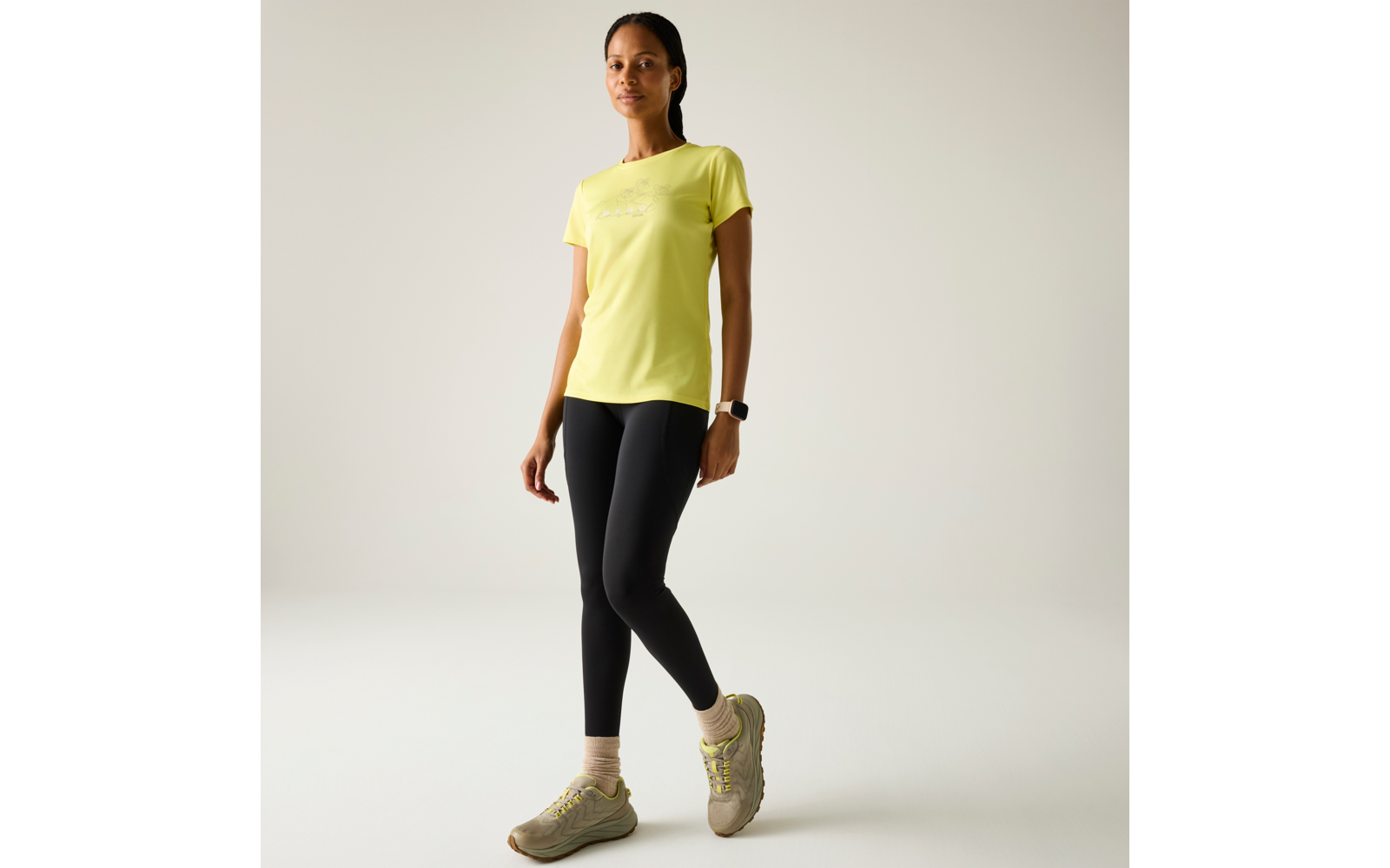 Personne debout en T‑shirt jaune, legging noir et baskets beiges sur fond clair
