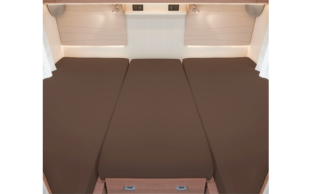 Trois matelas bruns côte à côte dans un lit de camping-car avec des rideaux blancs et des stores de fenêtre