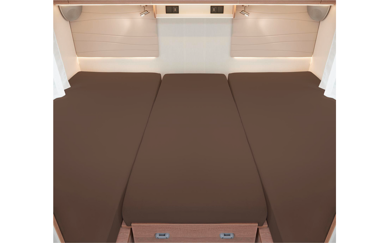 Trois matelas bruns côte à côte dans un lit de camping-car avec des rideaux blancs et des stores de fenêtre