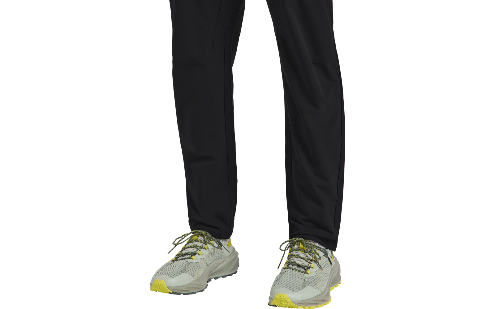 Beine in schwarzen Hosen und grauen Sportschuhen mit gelben Schnürsenkeln