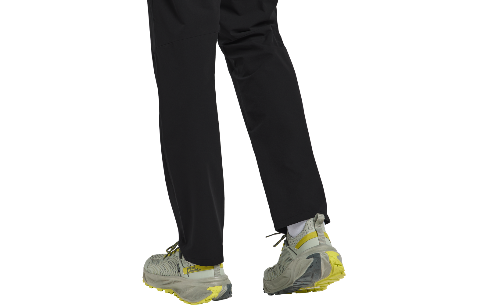 Beine einer Person in schwarzen Hosen und grauen Sportschuhen mit gelben Akzenten auf weißem Hintergrund