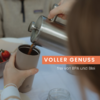 Hände gießen eine dunkle Flüssigkeit aus einer Edelstahlkanne in einen Thermobecher; im Hintergrund Glas, eine Schale mit einer Tomate und eine unscharfe Person; Schriftzug 'VOLLER GENUSS' und 'frei von BPA und Blei'
