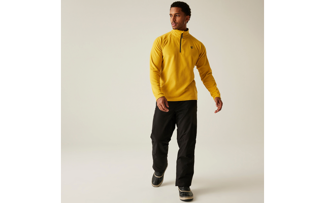 Mann trägt gelbes Sweatshirt und schwarze Hose, steht vor weißem Hintergrund
