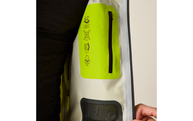 Innenansicht einer Jacke mit neon-gelber Innentasche, schwarzem Reißverschluss, vier Pflegepiktogrammen auf der Tasche, transparentem Fach mit grauem Rahmen und rechter Hand, die den Jackensaum hält; schwarzer Ärmel sichtbar