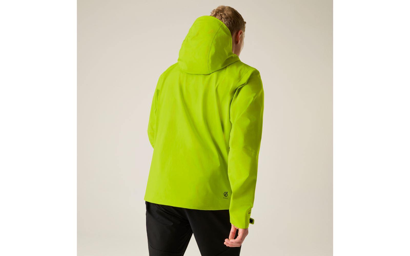 Person von hinten in neon-gelbgrüner Kapuzenjacke und schwarzer Hose vor hellem Hintergrund