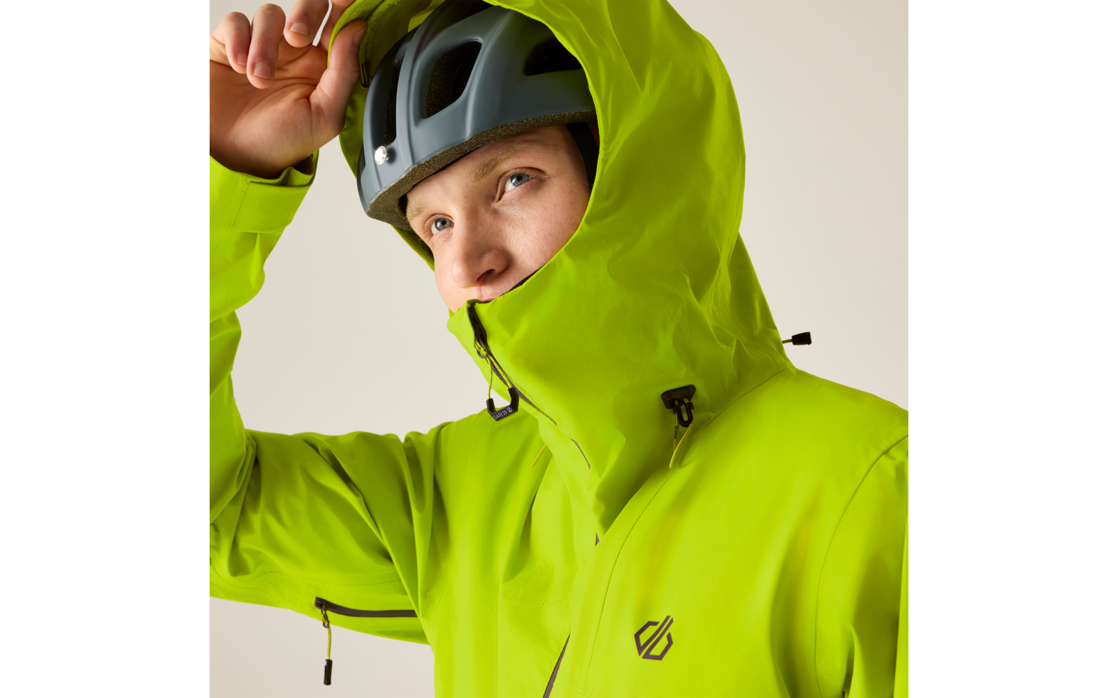 Person in heller grüner Kapuzenjacke und Helm, Hand an der Kapuze, Gesicht teilweise sichtbar, heller Hintergrund