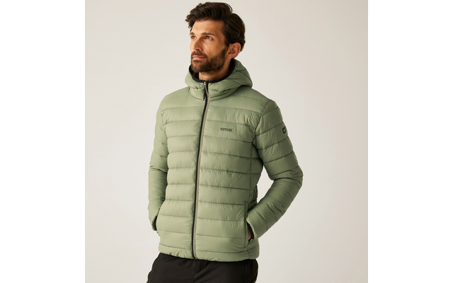 Mann mit kurzem braunem Haar und Bart trägt eine grüne Steppjacke und schwarze Hose vor hellem Hintergrund