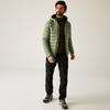 Ein Mann trägt eine grüne Steppjacke, schwarzen Hose und schwarze Schuhe, stehend vor hellem Hintergrund
