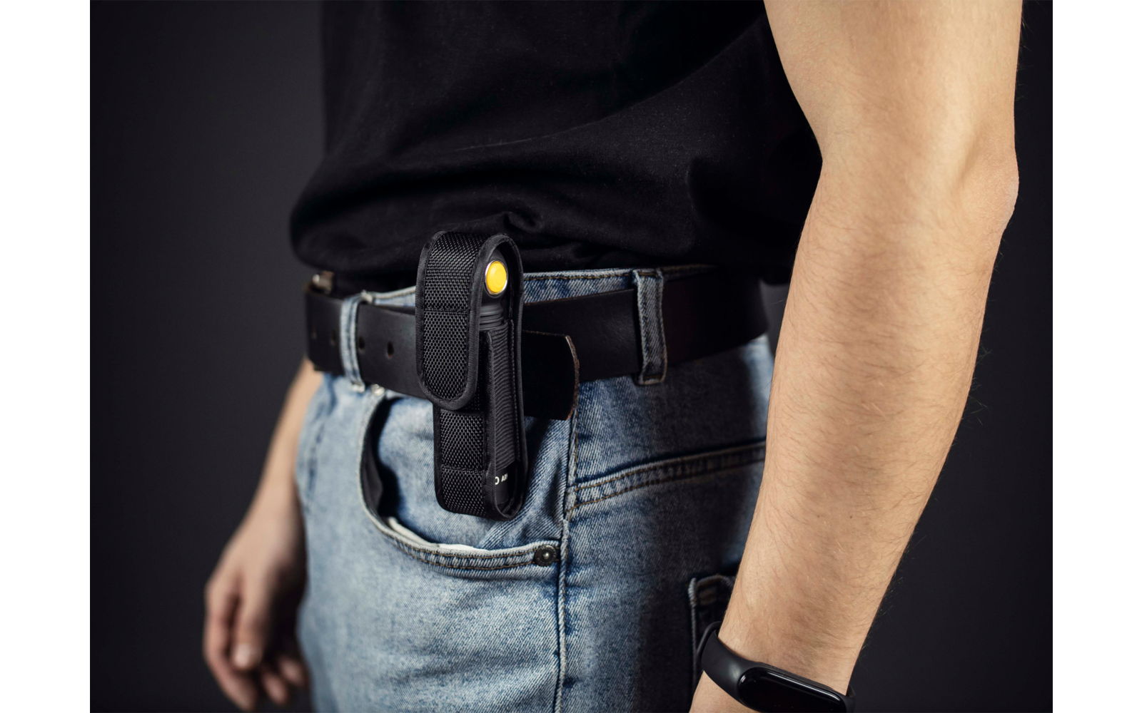 Oberkörper einer Person mit schwarzem Hemd, blauer Jeans und Pistole im Holster am Gürtel