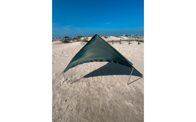 Grüne, dreieckige Plane auf zwei Stangen auf sandigem Strand; Dünen, Gebäude und blauer Himmel im Hintergrund