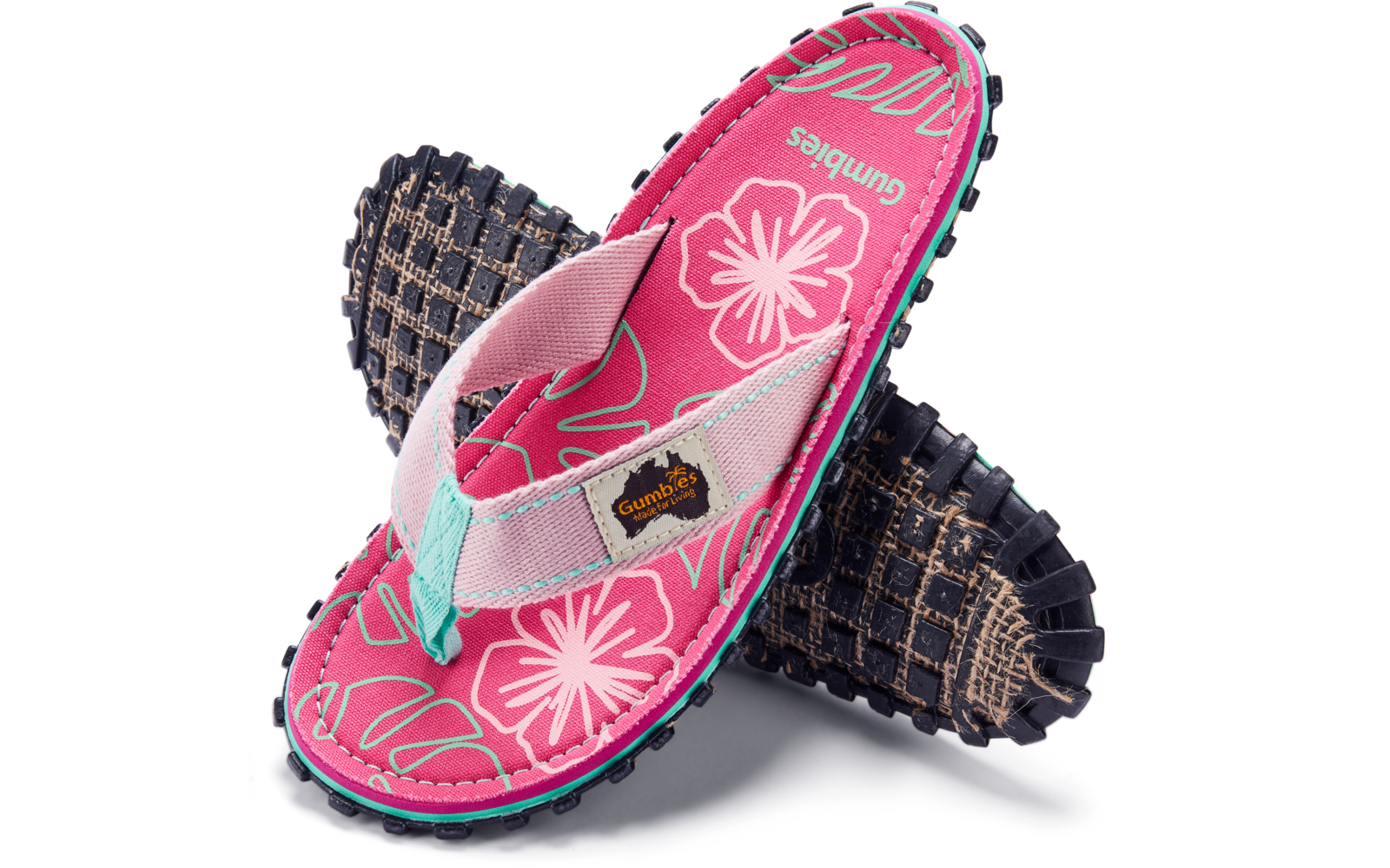 Zwei Flip-Flops übereinander, obere mit pinkem Fußbett mit weißen Blüten, hellrosa Riemen mit türkisfarbenem Zehensteg, schwarze Profilsohlen mit Noppen, Stoffetikett mit Aufdruck "Gumbies"