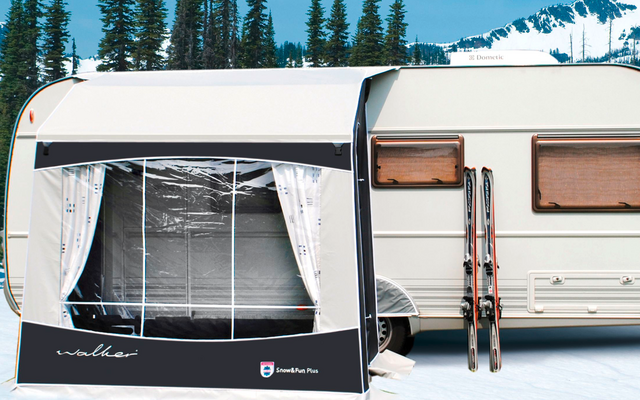 Caravan with attached awning in a snowy landscape, trees and mountains in the background