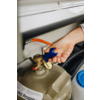 Hand dreht blauen Ventilgriff an grauer Flasche mit Aufschrift 'Propan' in einem Schrank