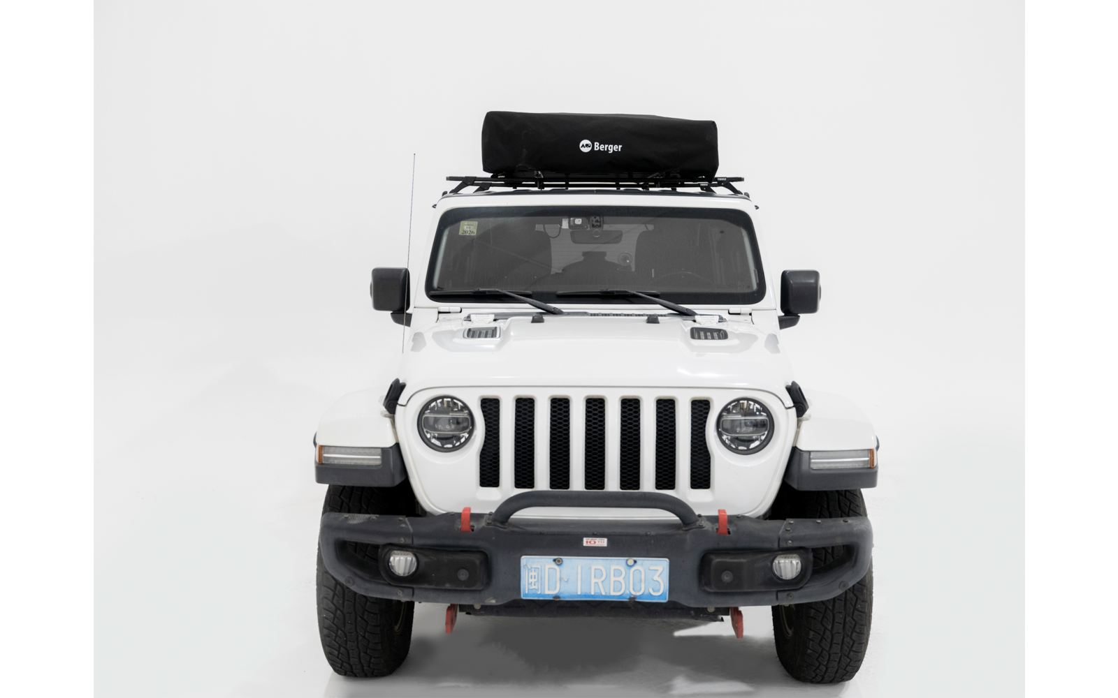 Frontaufnahme eines weißen Geländewagens vor weißem Hintergrund. Schwarzer Dachträger mit schwarzer Tasche, runde Scheinwerfer, schwarze Stoßstange, sichtbares blaues Kennzeichen