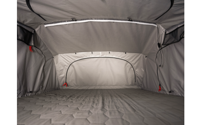 Innenraum eines grauen Zeltes mit gepolsterter Liegefläche, gewölbter Decke, Reißverschlüssen und roten Zugbändern