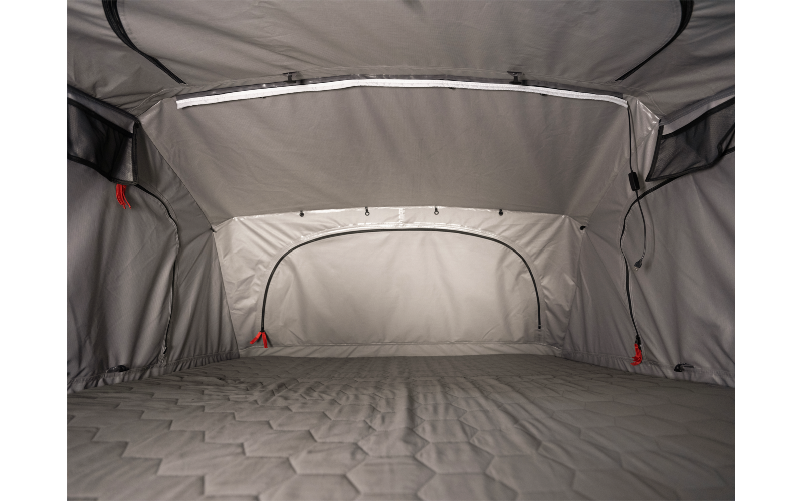 Innenraum eines grauen Zeltes mit gepolsterter Liegefläche, gewölbter Decke, Reißverschlüssen und roten Zugbändern