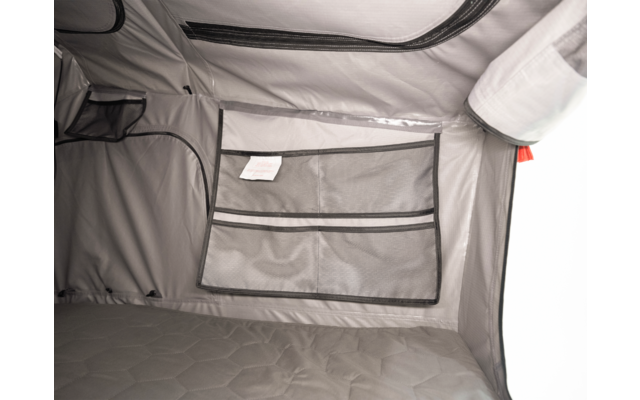 Graue Stoffwände mit Reißverschlüssen, aufgenähte Netztasche mit kleinem Etikett und gesteppte Matratze