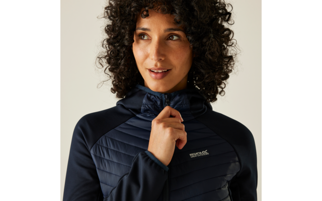 Person mit dunklen, lockigen Haaren, schaut nach rechts, trägt eine dunkelblaue gesteppte Jacke mit Kapuze und hält den Reißverschlussgriff