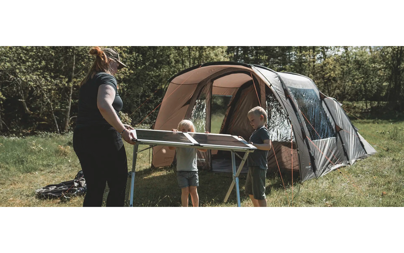 Person grillt an einem Holztisch vor einem Zelt im Wald