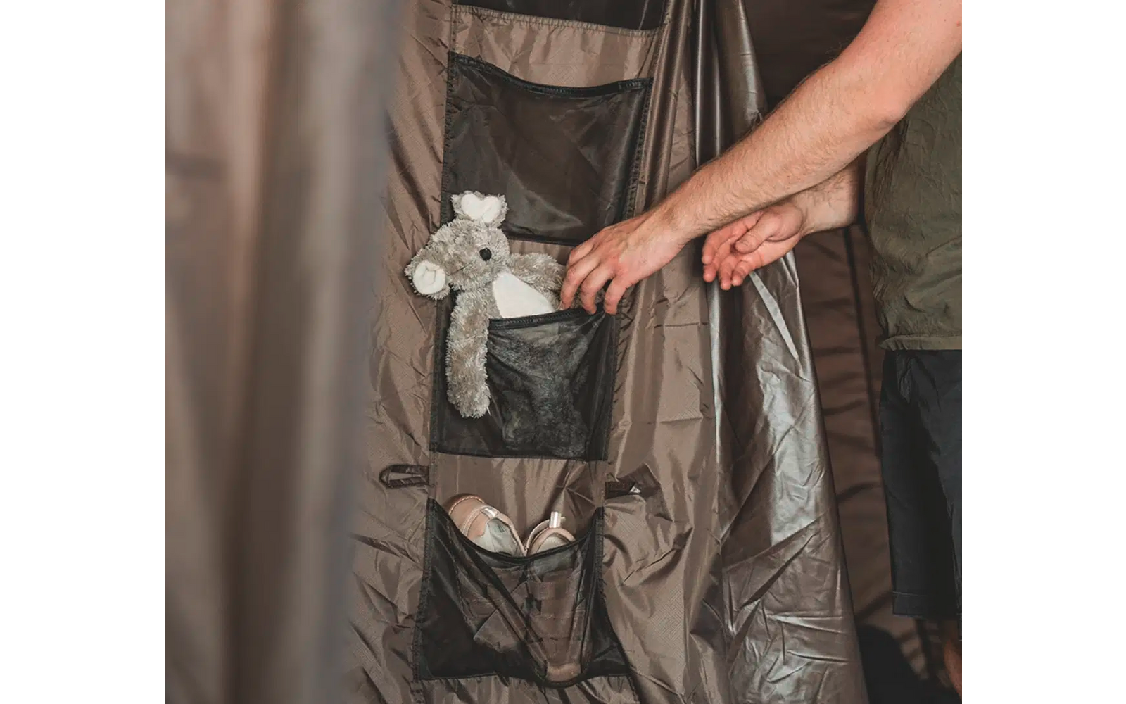 Eine Hand berührt eine braune Jacke mit einem grauen Stofftier in der Innentasche