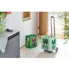 Deux caisses en plastique vertes contenant des bouteilles en verre dans un hall près d'une porte d'entrée ouverte ; une caisse sur un petit chariot à roulettes avec poignée déployée ; plante en pot et meuble avec un vase et des clés visibles