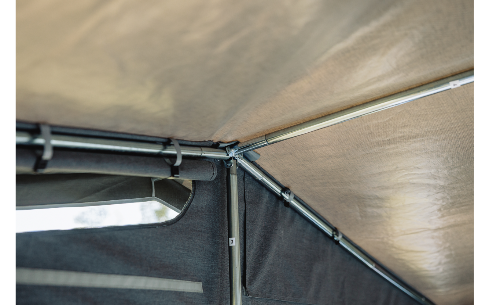 Beige Stoffdach und dunkle Seitenwand, Metallstangen mit Eckverbindern, rechteckige Öffnung mit Lichteinfall