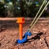 Blauer Handschaufel mit orangem Griff steckt in Erde, im Hintergrund grüne Pflanzen