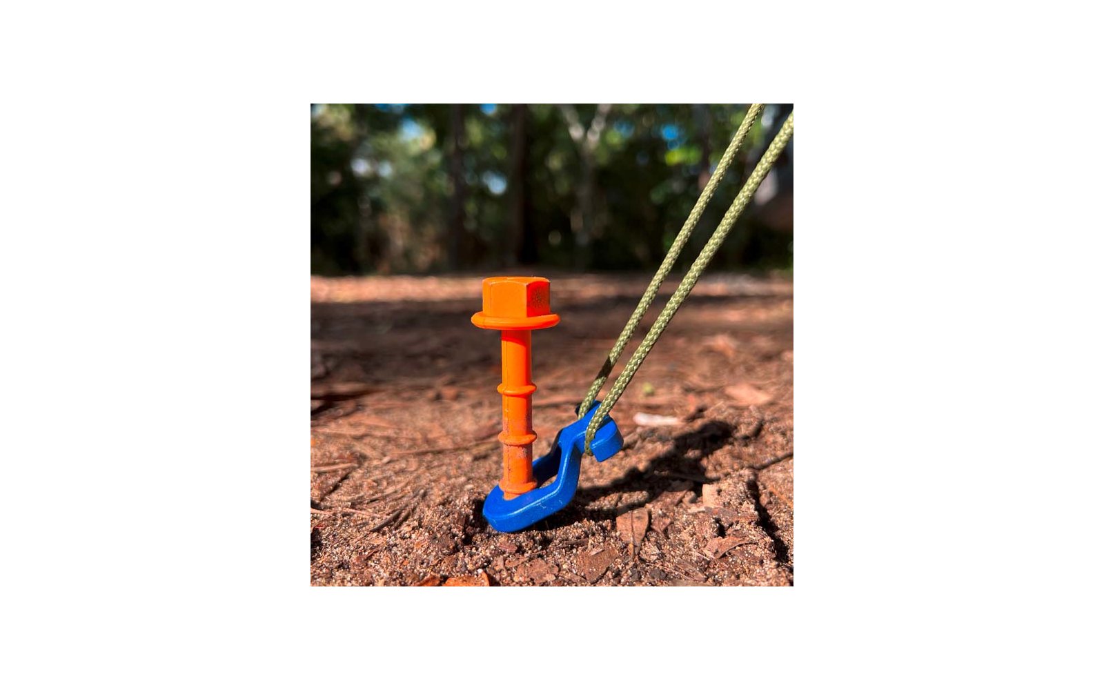 Blauer Handschaufel mit orangem Griff steckt in Erde, im Hintergrund grüne Pflanzen