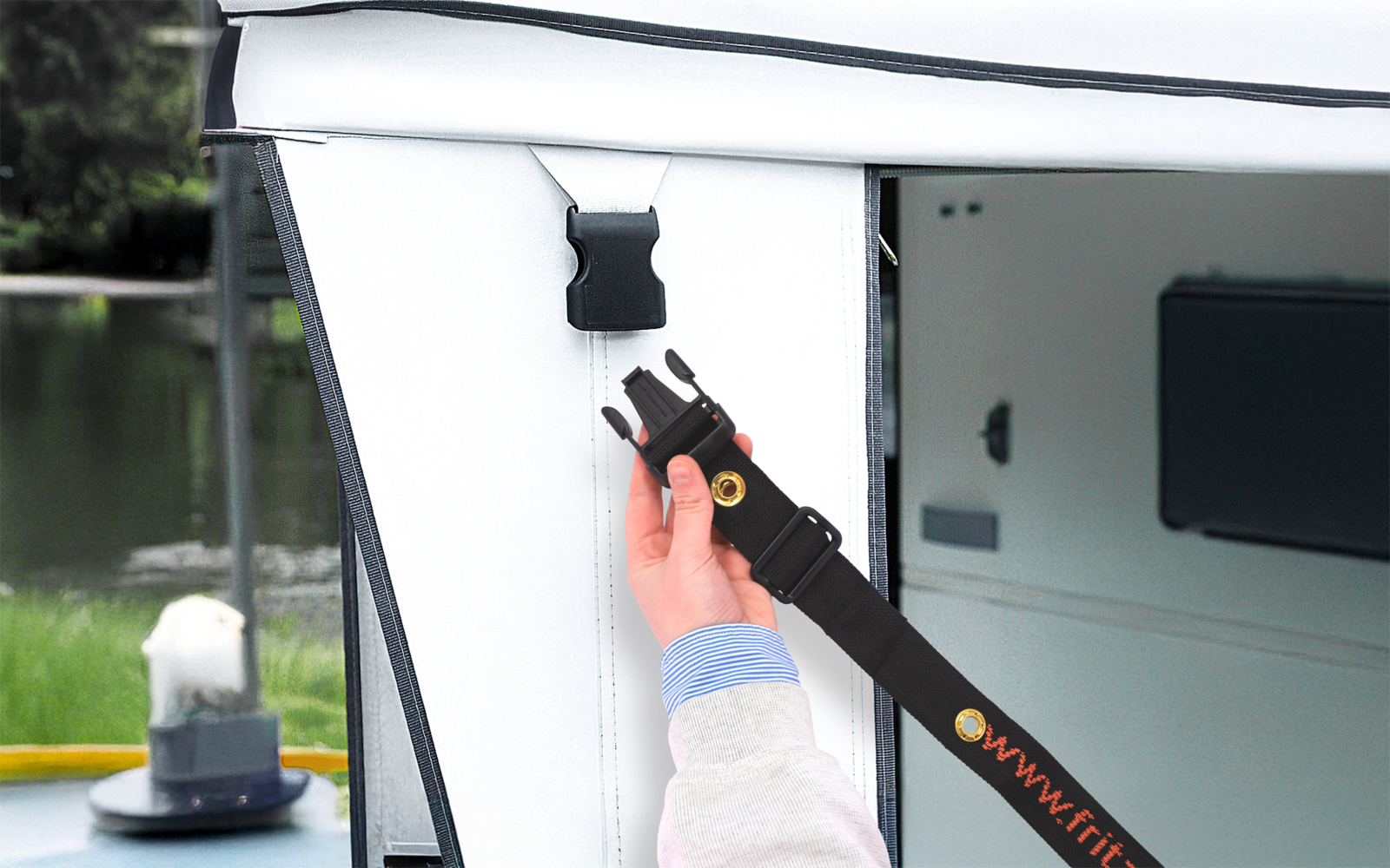 Hand mit hellem Ärmel befestigt schwarzen Gurt mit Steckschloss an weißem Stoffpanel; im Hintergrund Wasser, Gras und ein Poller