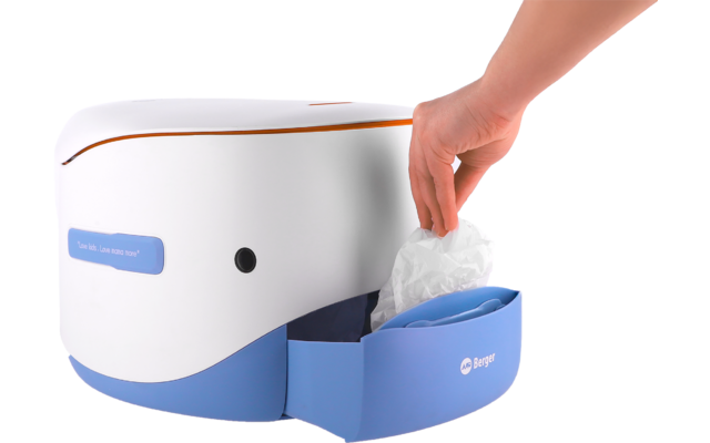 Weiße und blaue Maschine auf einem Tisch, blaues Fach geöffnet, Hand nimmt ein weißes Einwegpad heraus