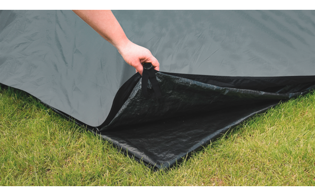 Mano che tiene un angolo di una tenda nera su erba verde