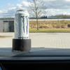 Weiße Getränkedose steht auf schwarzer Halterung im Auto vor einer Parkfläche und Feld
