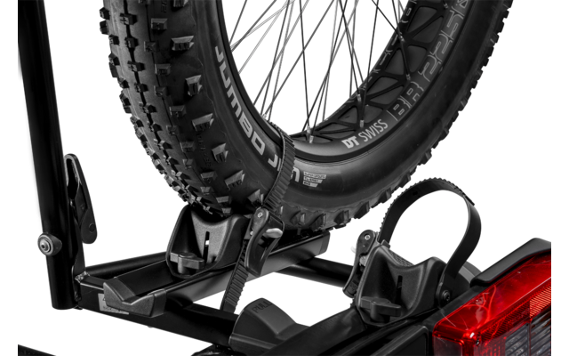Rueda de bicicleta con neumático de tacos situada en un soporte de plástico de un portabicicletas trasero, luz trasera roja del vehículo visible abajo a la derecha