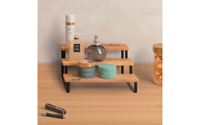 Dreistufiges Holzregal mit schwarzen Metallfüßen auf hellem Holztisch, darauf eine runde Glasflasche, eine rechteckige Flasche, eine hohe Sprühdose und zwei grüne Tiegel; rechts ein Glasbehälter mit orangefarbenen Kapseln; vorne links zwei schlanke S