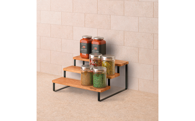 Dreistufiges Holzregal mit schwarzem Metallgestell vor beige gekachelter Wand; oben zwei hohe Glasgefäße mit roten Inhalten und dunklen Etiketten, auf den unteren Stufen drei kleinere Glasgefäße mit grünen, mehrfarbigen und gelblichen Inhalten, alle 