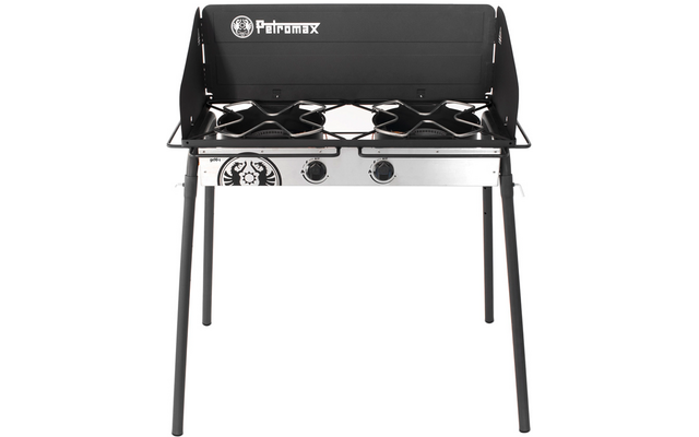 Zweiflammiger Kocher auf vier Beinen, schwarzer Windschutz mit 'Petromax'-Logo, zwei runde Brenner mit Topfträgern und zwei Drehreglern auf silberner Blende